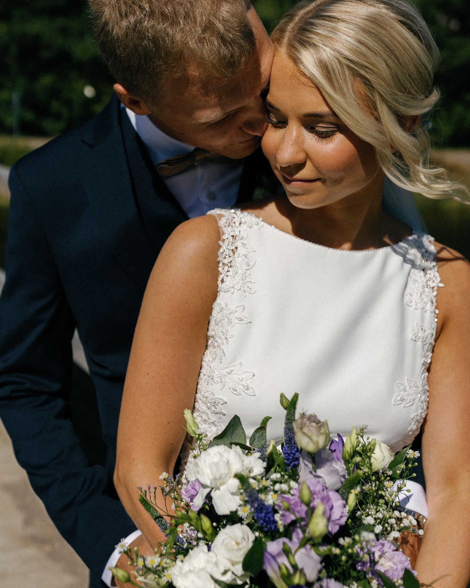 Romantic wedding portrait showing details of a white lace dress and purple floral bouquet.