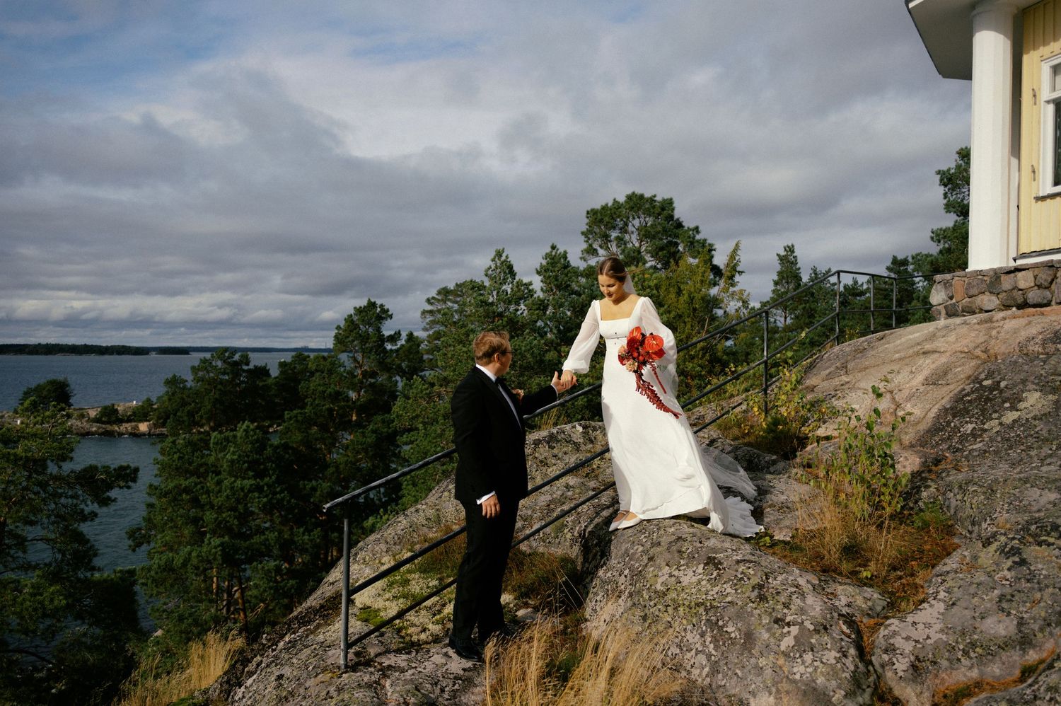 Wedding couple poses on scenic rocky cliffs overlooking a lake with dramatic cloudy skies in the background.