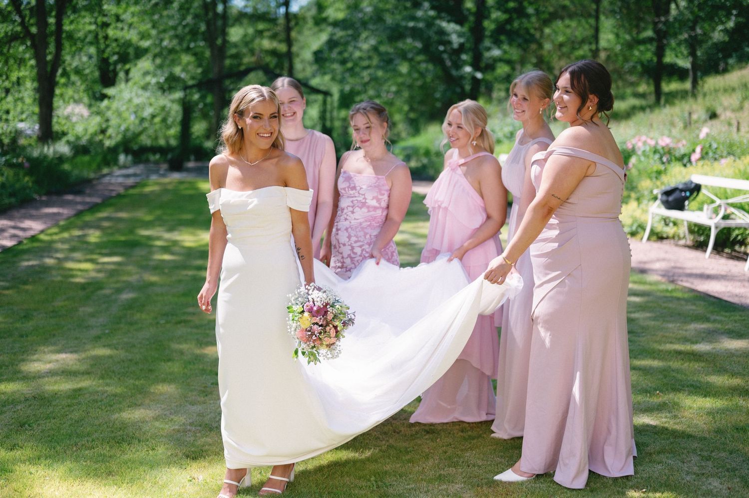 Wedding party poses together on grass with bridesmaids in light pink dresses and white gowns.
