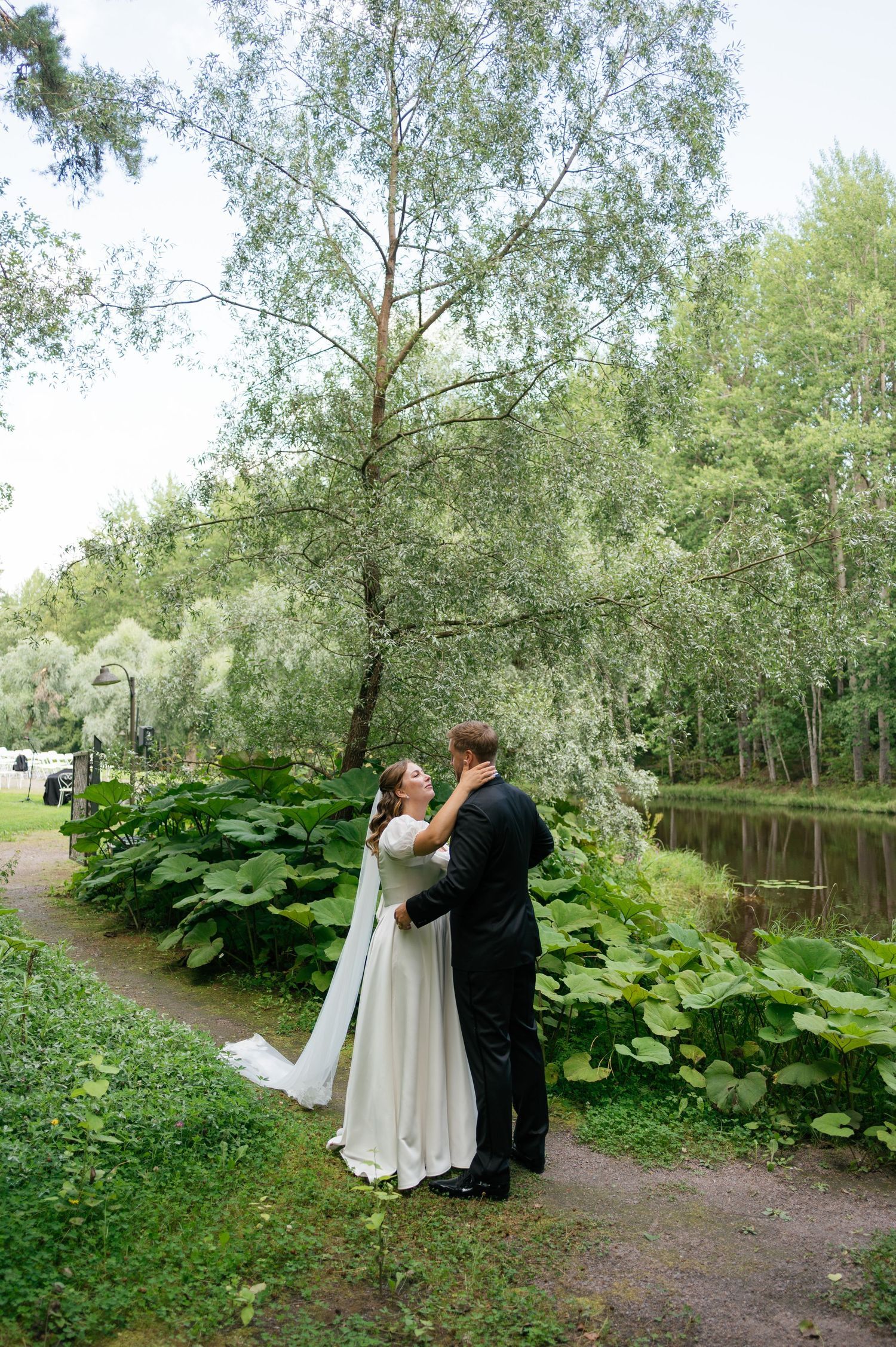 A romantic moment between newlyweds on a garden path beside a serene pond.