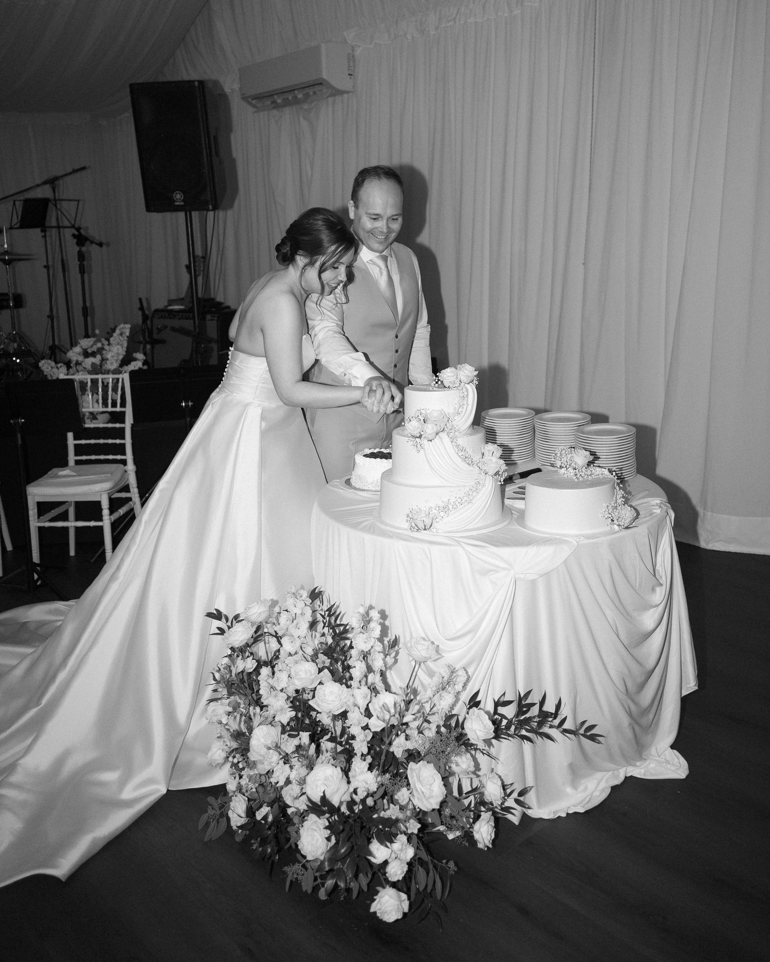 Black and white photo of bride and groom cutting their wedding cake at elegant reception.
