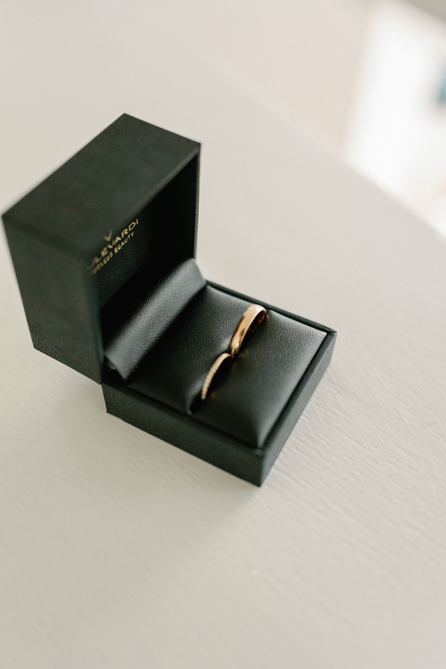 Two elegant gold wedding bands displayed in an open black luxury ring box on a white surface.