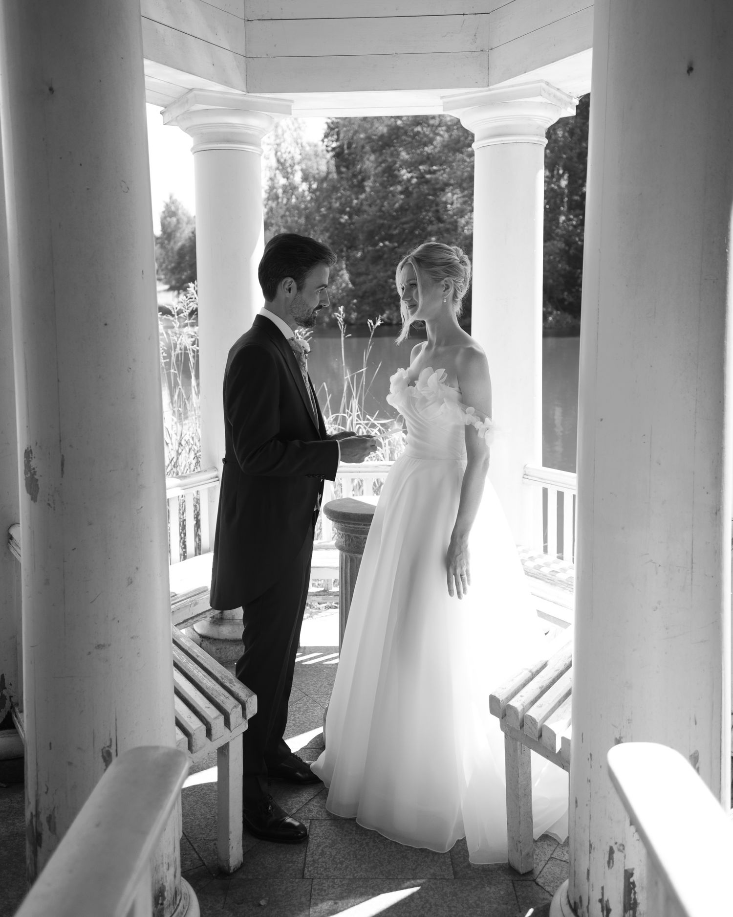 Black and white photo of a bride and groom exchanging vows in an elegant white gazebo on their wedding day.