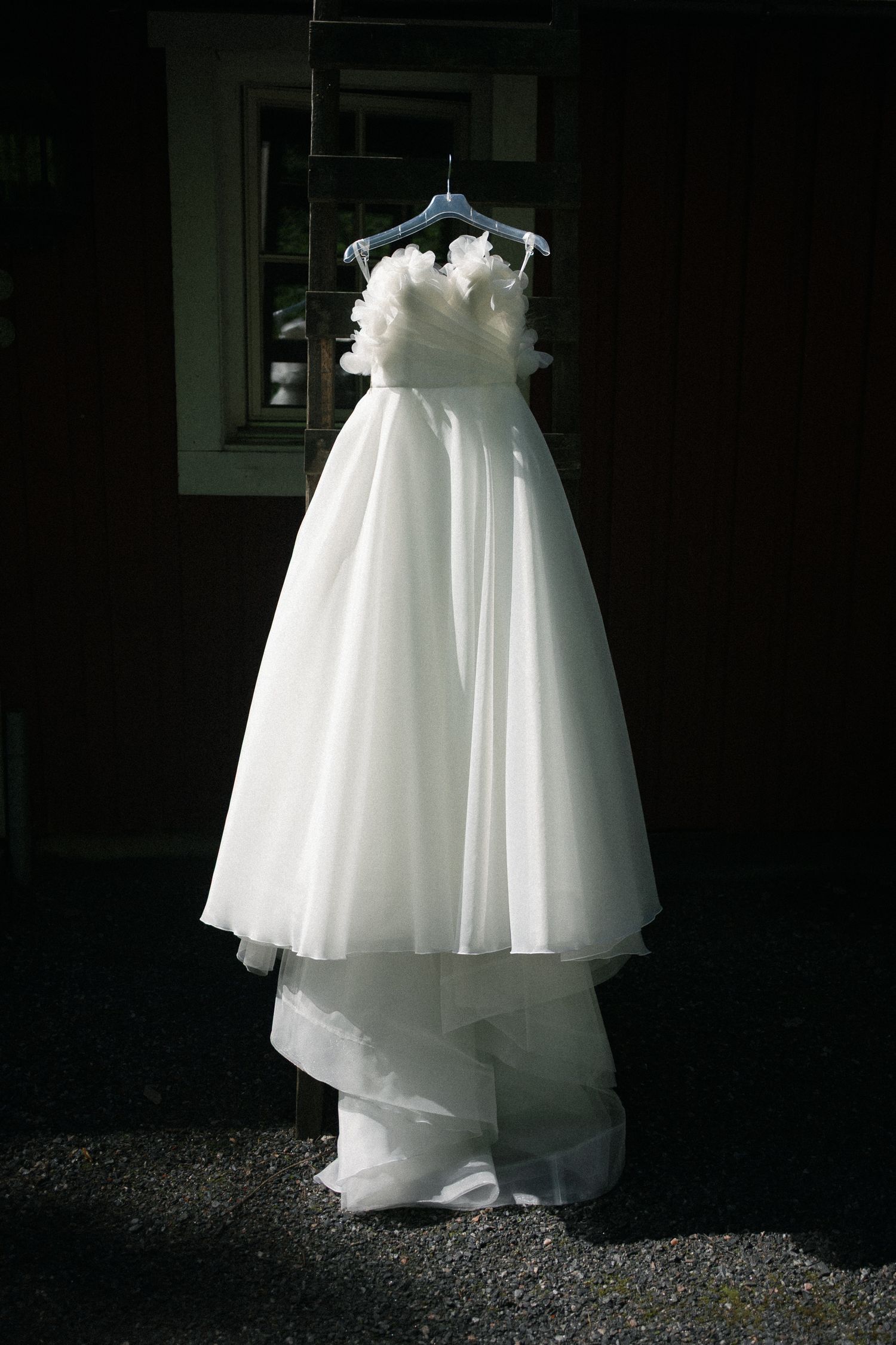 Elegant white strapless ball gown wedding dress with floral bodice detail hanging on hanger against dark background.
