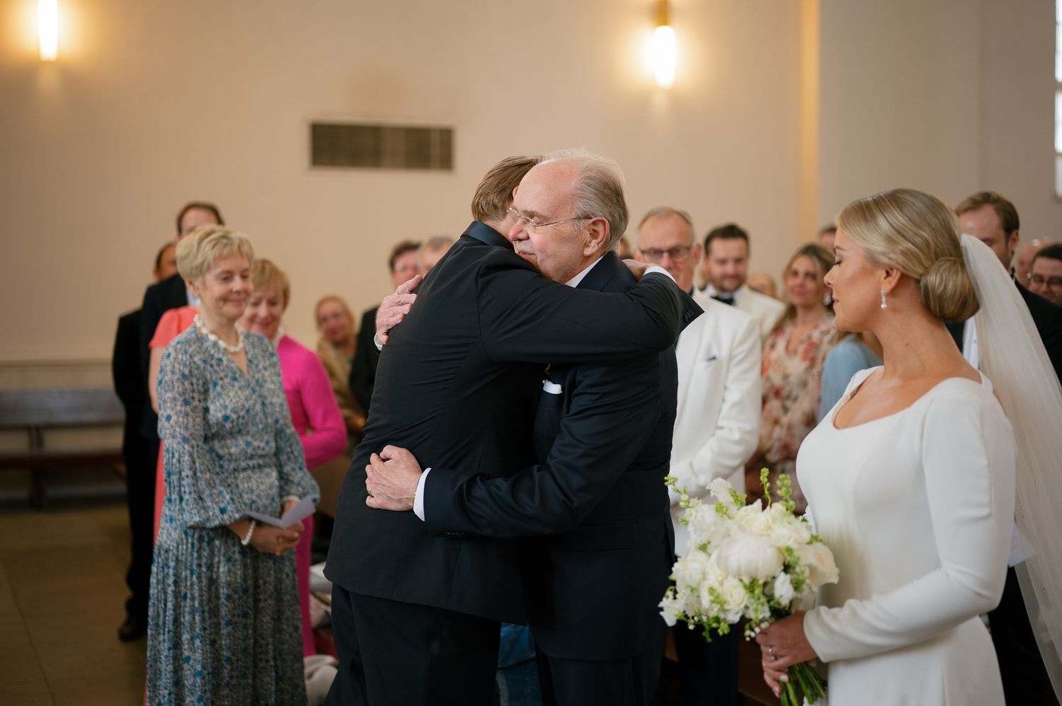 An emotional embrace during a wedding ceremony with guests looking on in a church setting.
