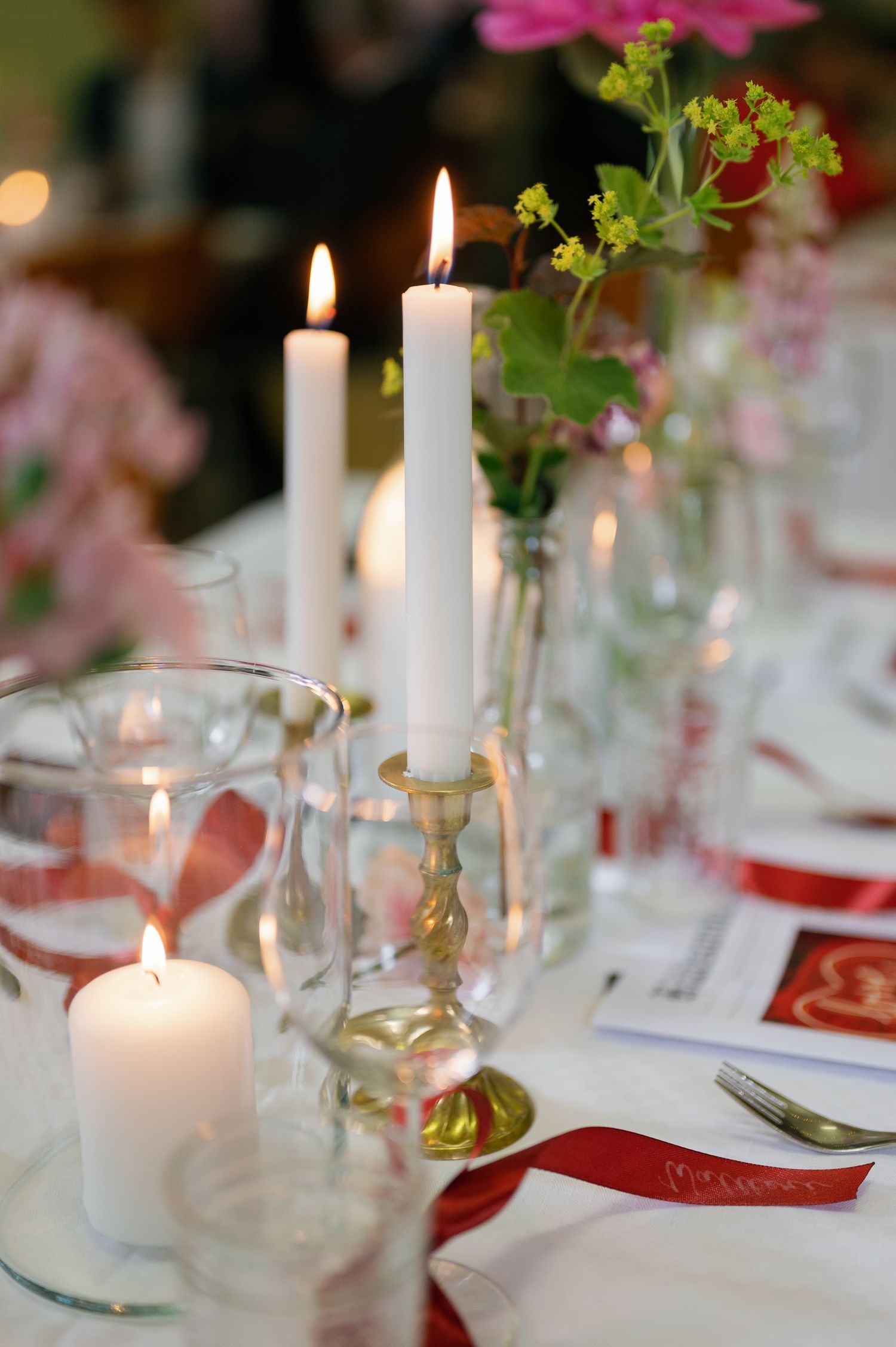 Elegant wedding reception table with white candles, glassware and pink floral centerpieces.