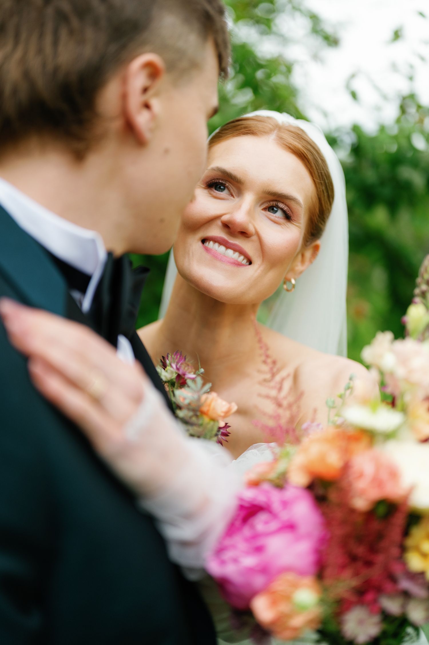 Newlyweds share tender glances while holding vibrant pink and orange bouquet.