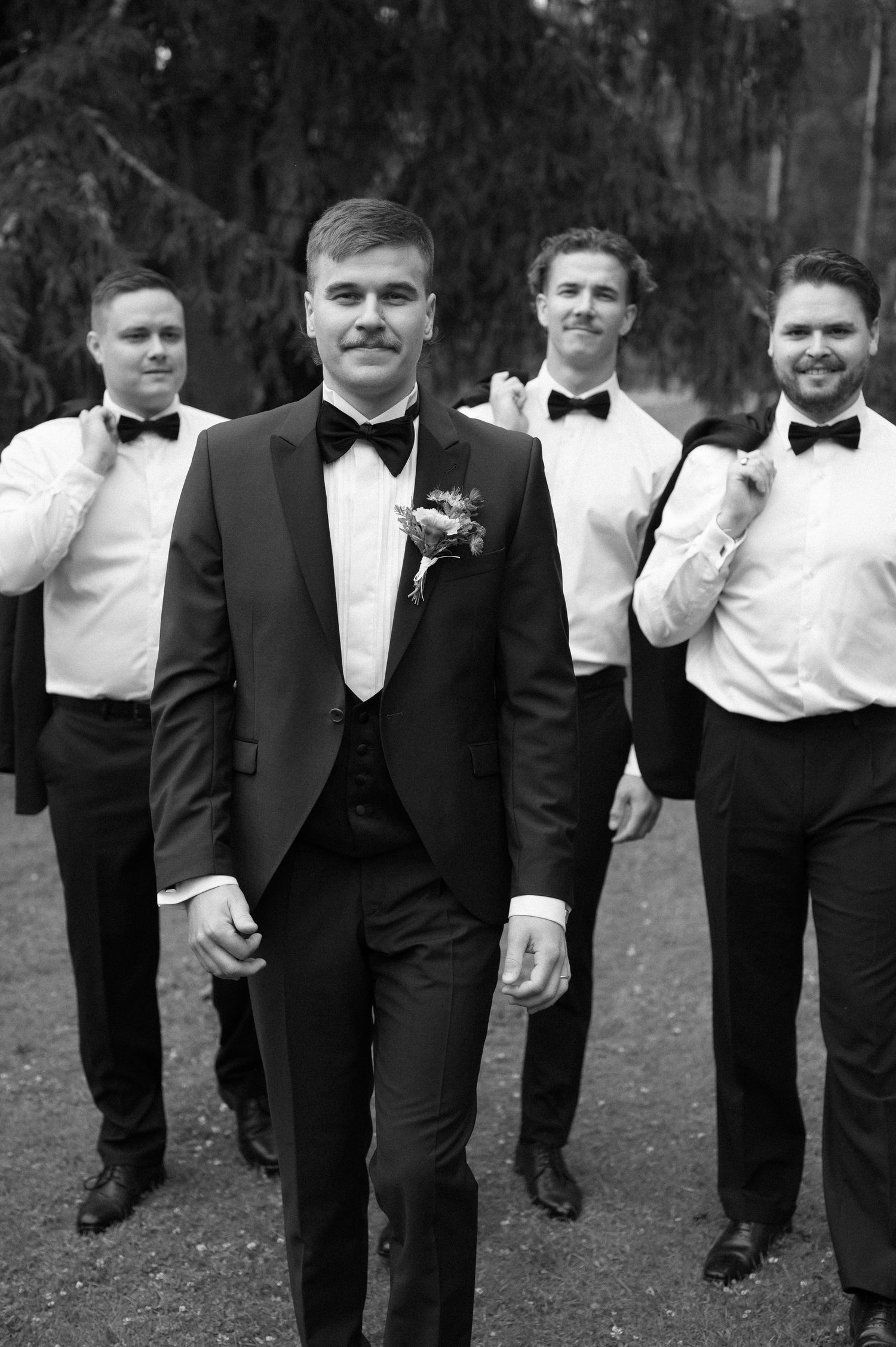 Groomsmen in black tuxedos and bowties pose together outdoors.