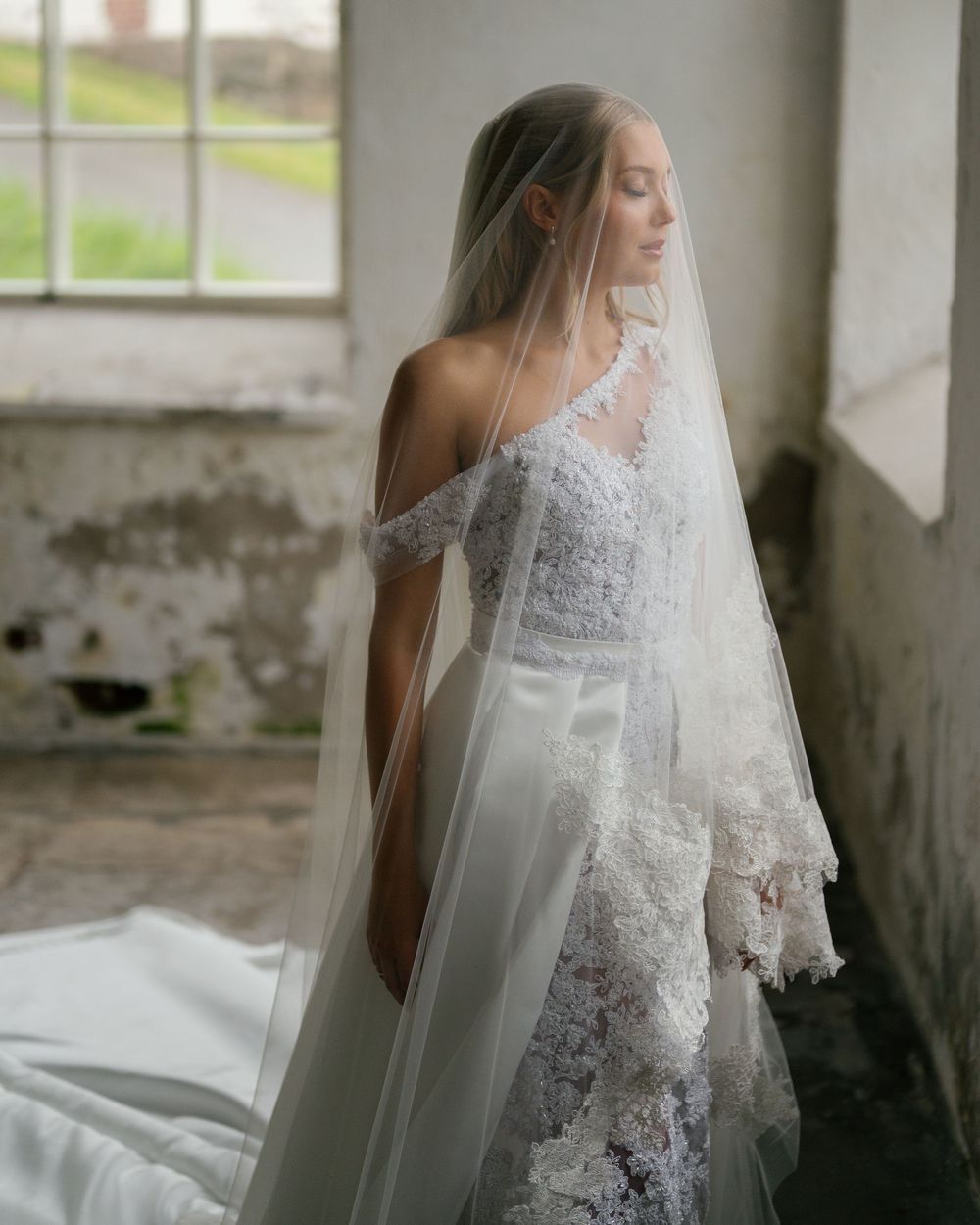 Romantic side profile of bride with flowing veil near window in vintage setting.