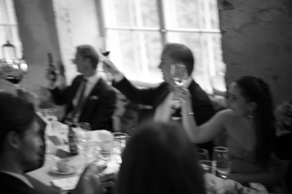 Black and white photo of wedding guests dancing and celebrating at an indoor reception.