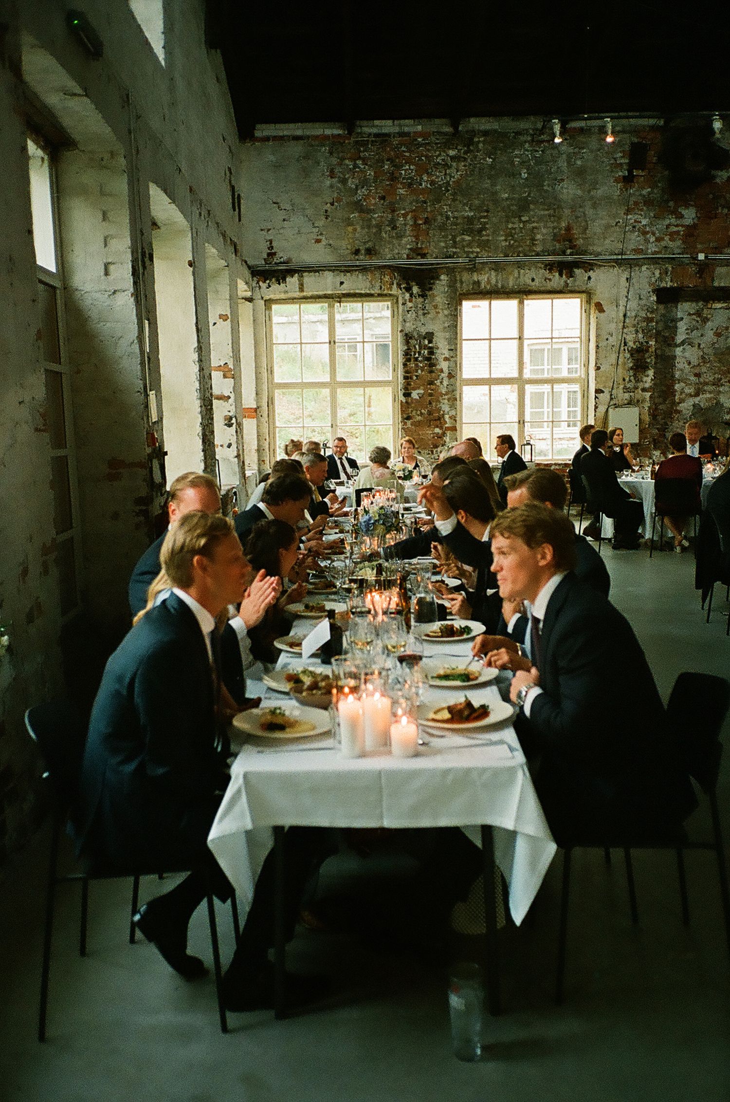 Wedding reception dinner in an industrial-style venue with exposed brick walls and large windows.