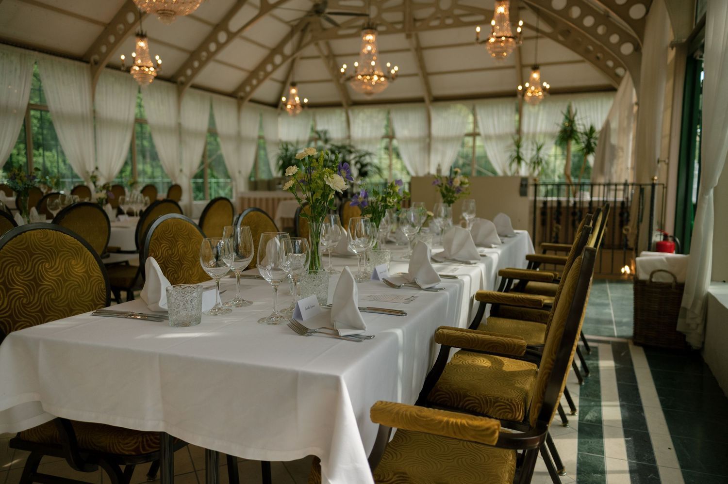 Elegant wedding reception venue with white tablecloths and hanging lights in a conservatory setting.