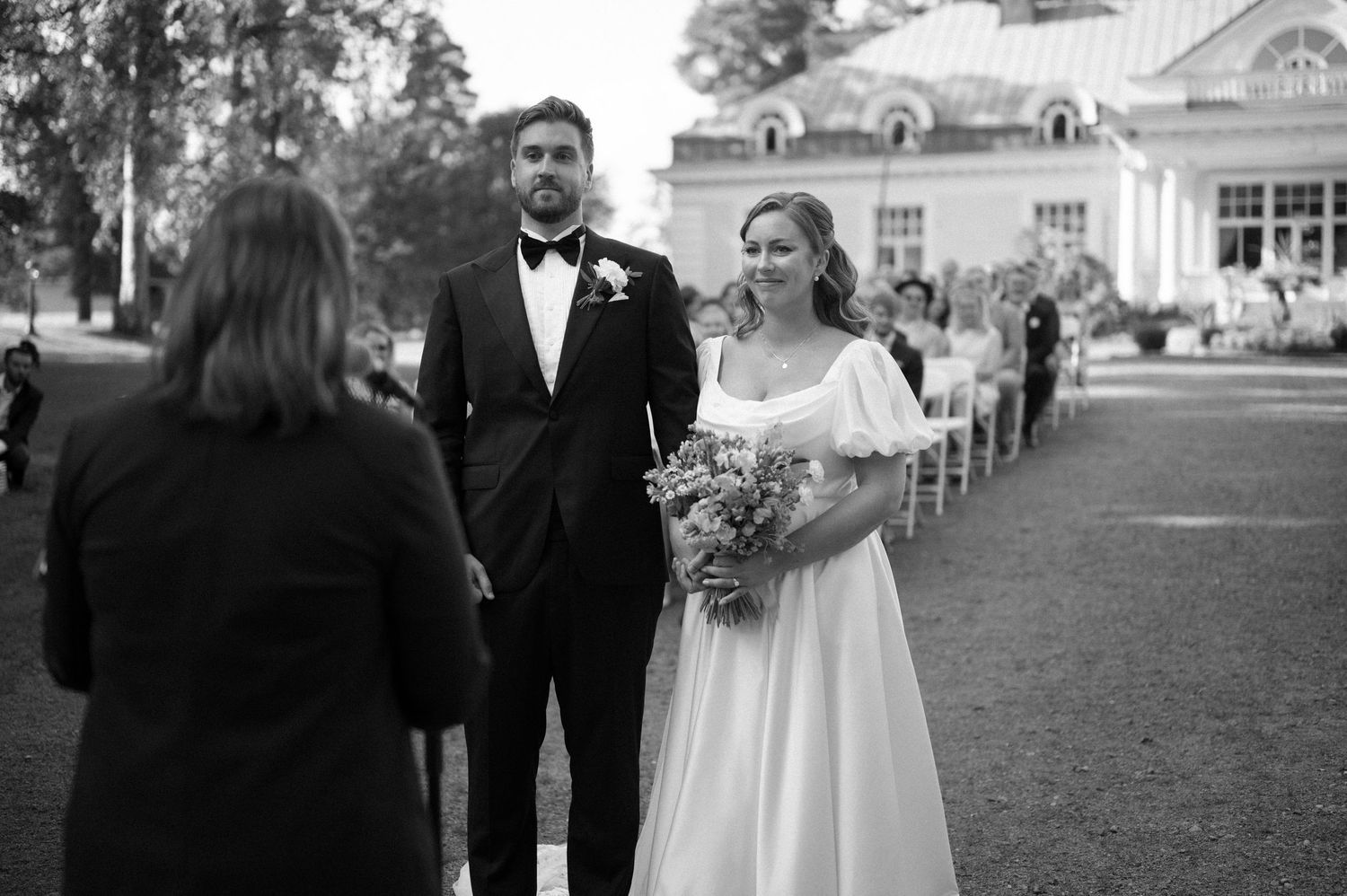Wedding ceremony processional on a gravel path with elegant venue building in the background.