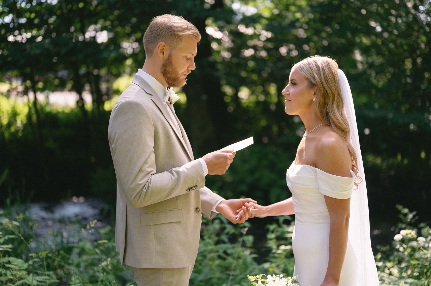 A couple shares a private moment while reading letters to each other in a sunlit forest setting.