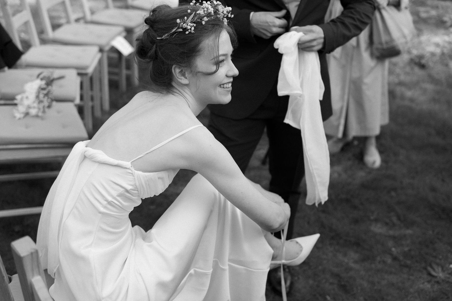 A black and white portrait of a bride in a flowing dress seated outdoors during the wedding celebration.