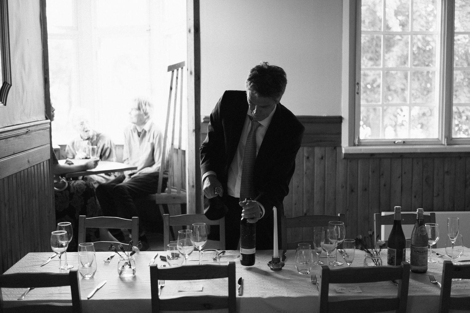 Black and white photo of a dining room being prepared with elegant table settings.