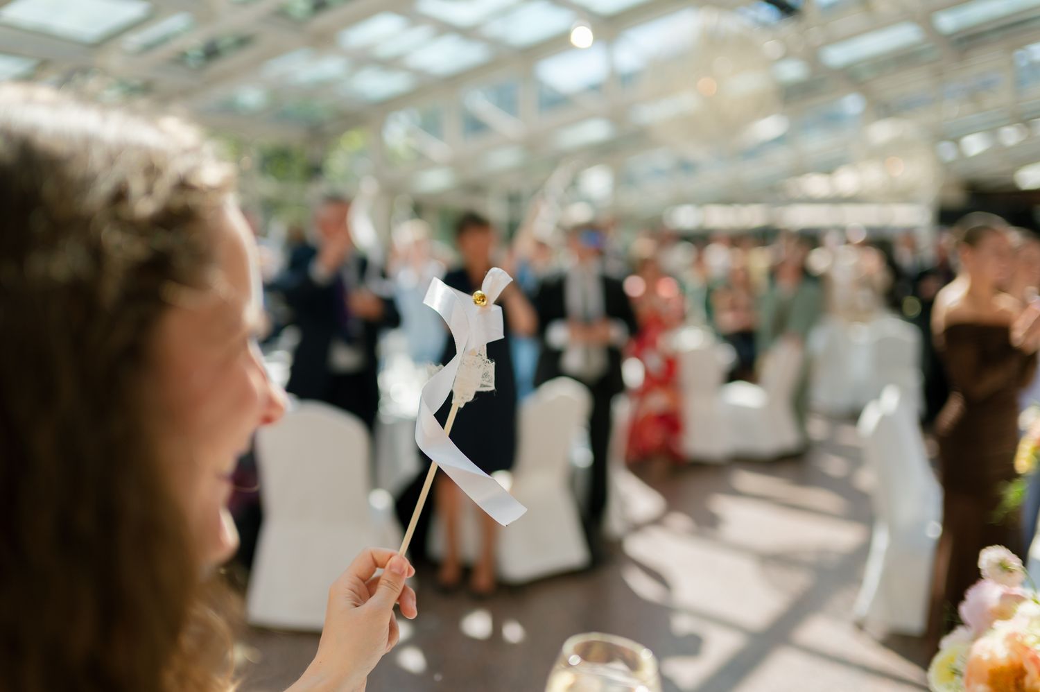 Guest holds a white horse-on-a-stick prop at an elegant wedding reception in a bright greenhouse venue.
