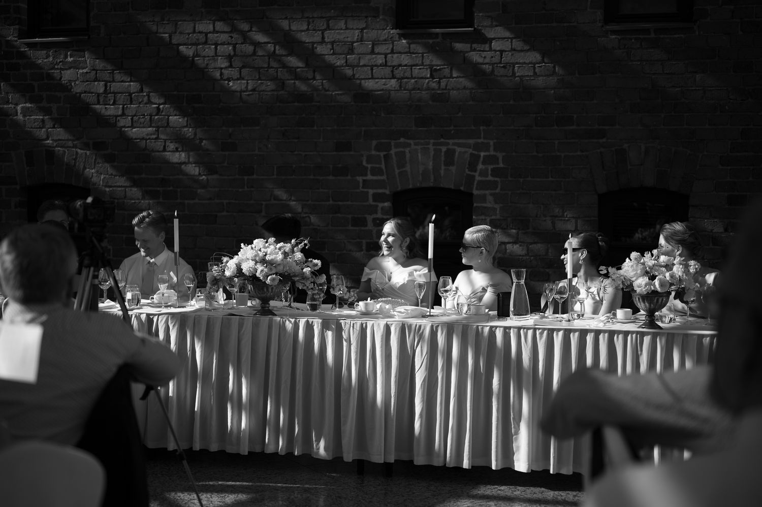 Black and white wedding reception photo showing bridal party seated at elegantly decorated head table in brick venue.