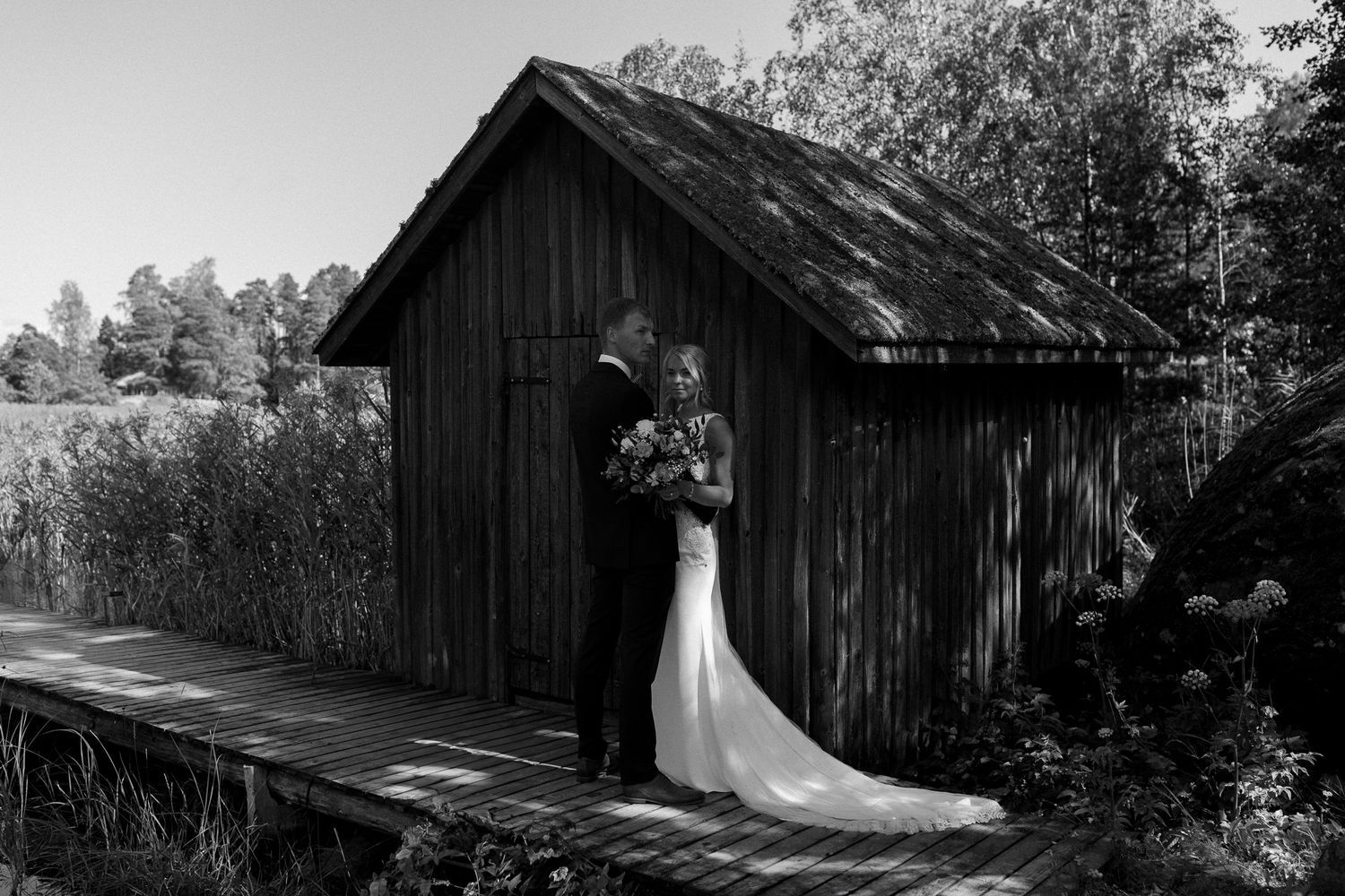 Wedding couple silhouetted against rustic barn buildings in dramatic black and white.