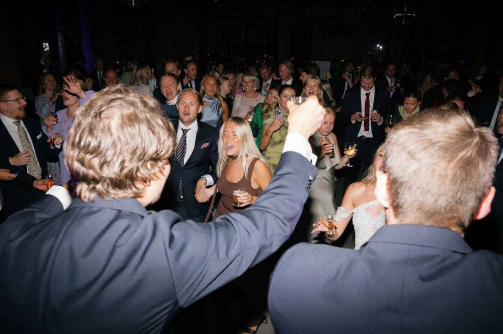 Wedding guests dance and celebrate on a crowded dance floor under dim lighting.