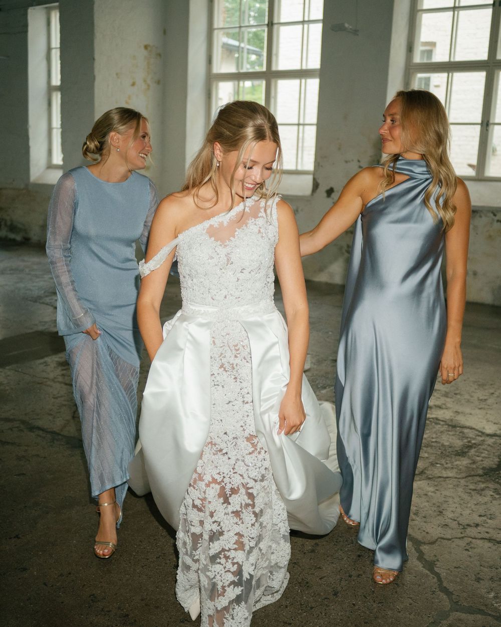 Bridesmaids in light blue dresses dance alongside a bride in a white lace gown at a wedding reception.
