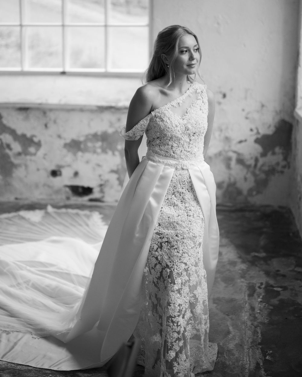 Elegant lace wedding dress details captured in black and white against weathered walls.