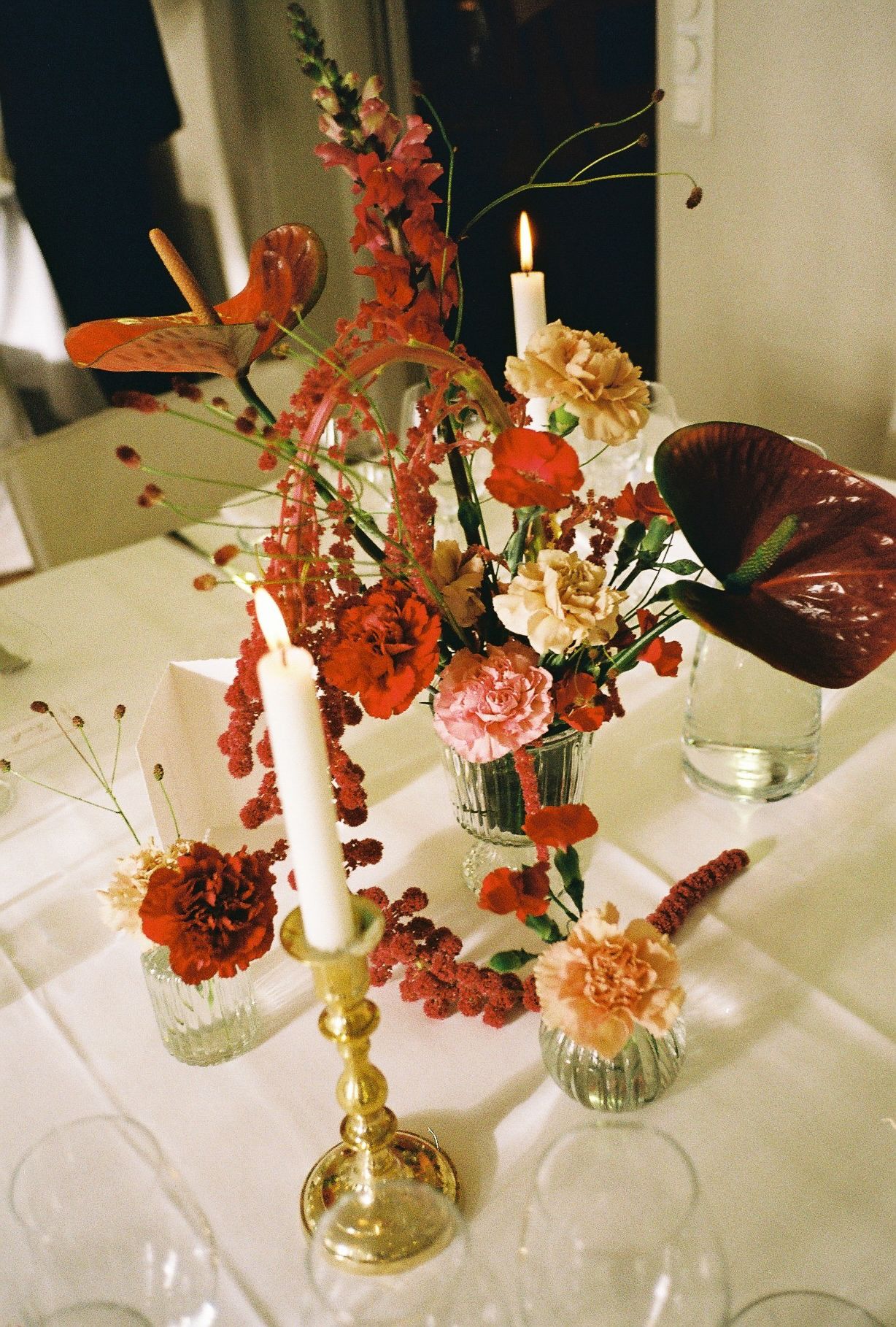 Elegant table setting with coral and peach flowers in glass vases and gold candlesticks on white tablecloth.
