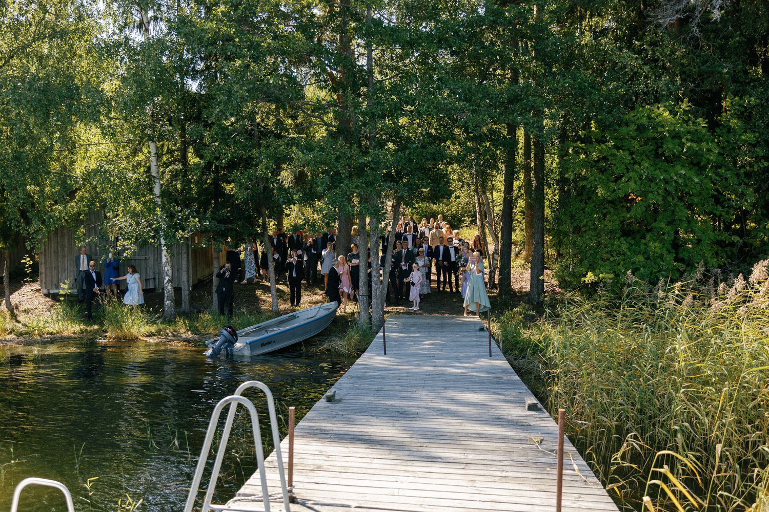 Wedding guests gather on a wooden dock pathway extending into a scenic lake.