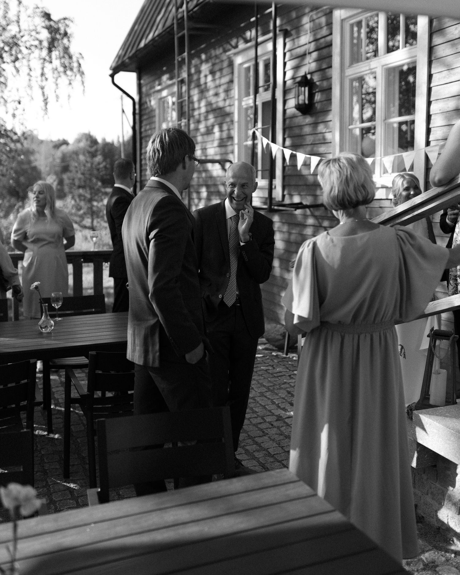 People standing on a porch of a rustic wooden house during an outdoor gathering.
