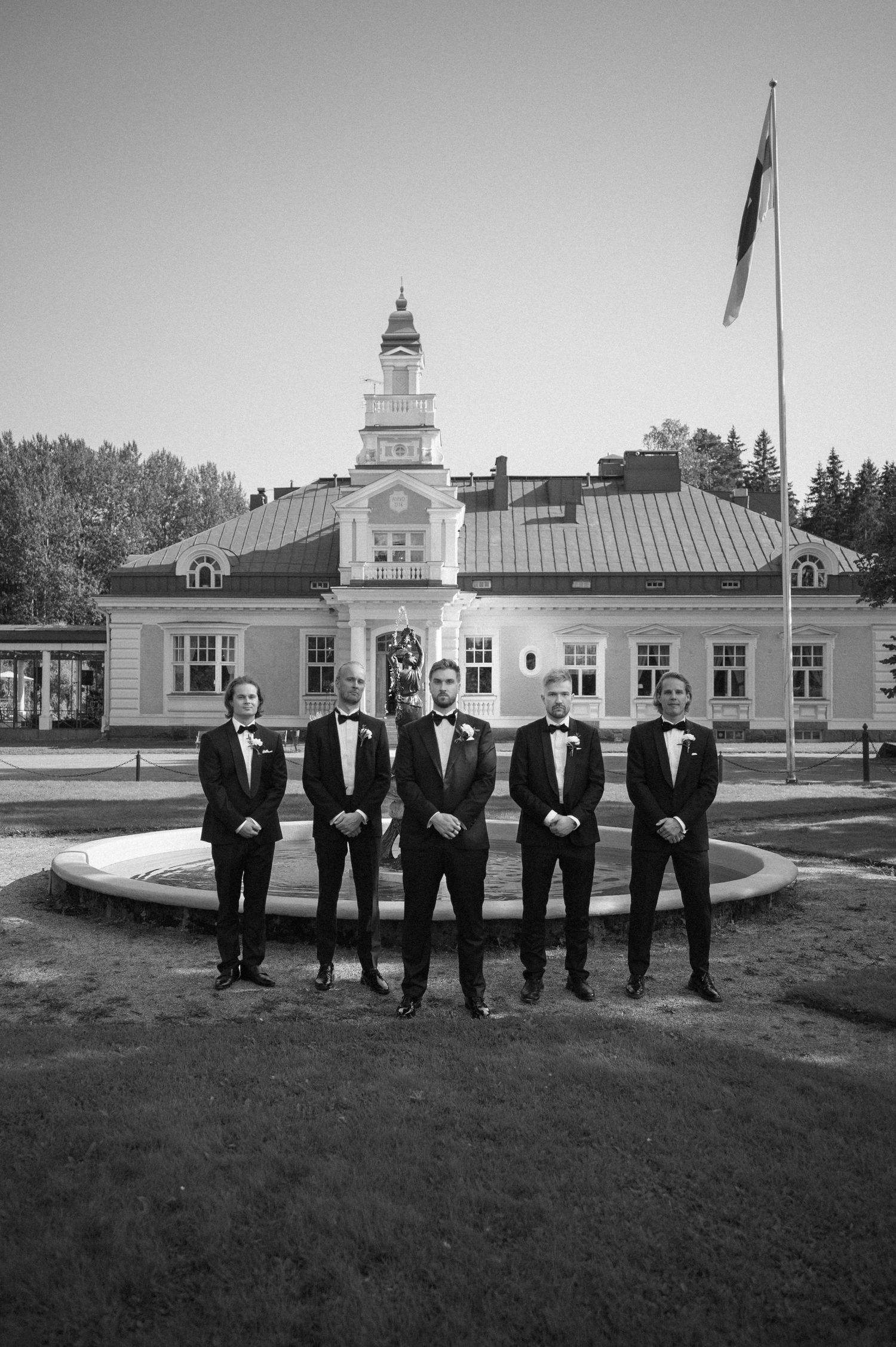 Black and white panorama of a historic building with formal group standing on lawn.