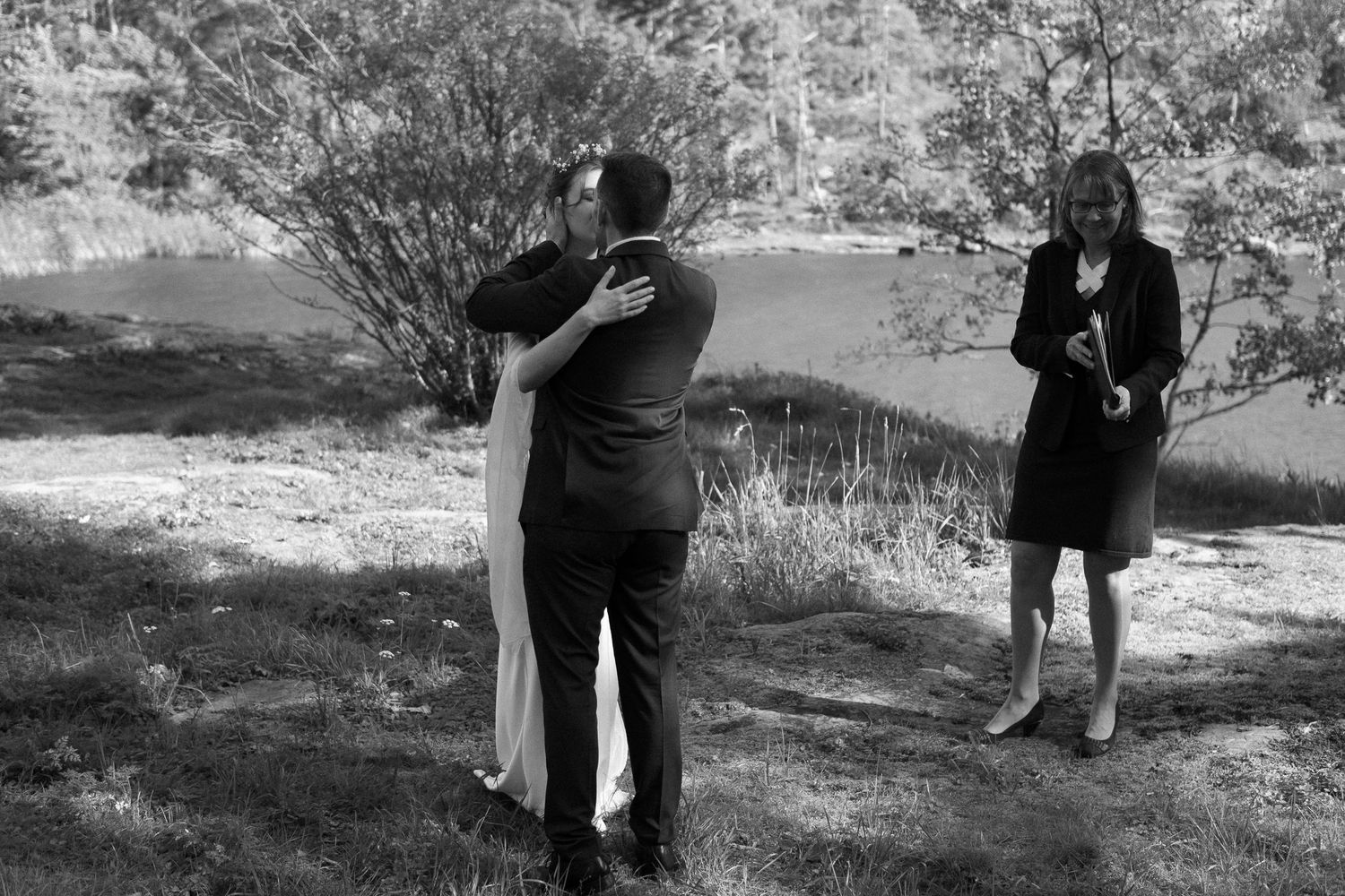 A black and white photo captures an intimate moment during an outdoor wedding ceremony.