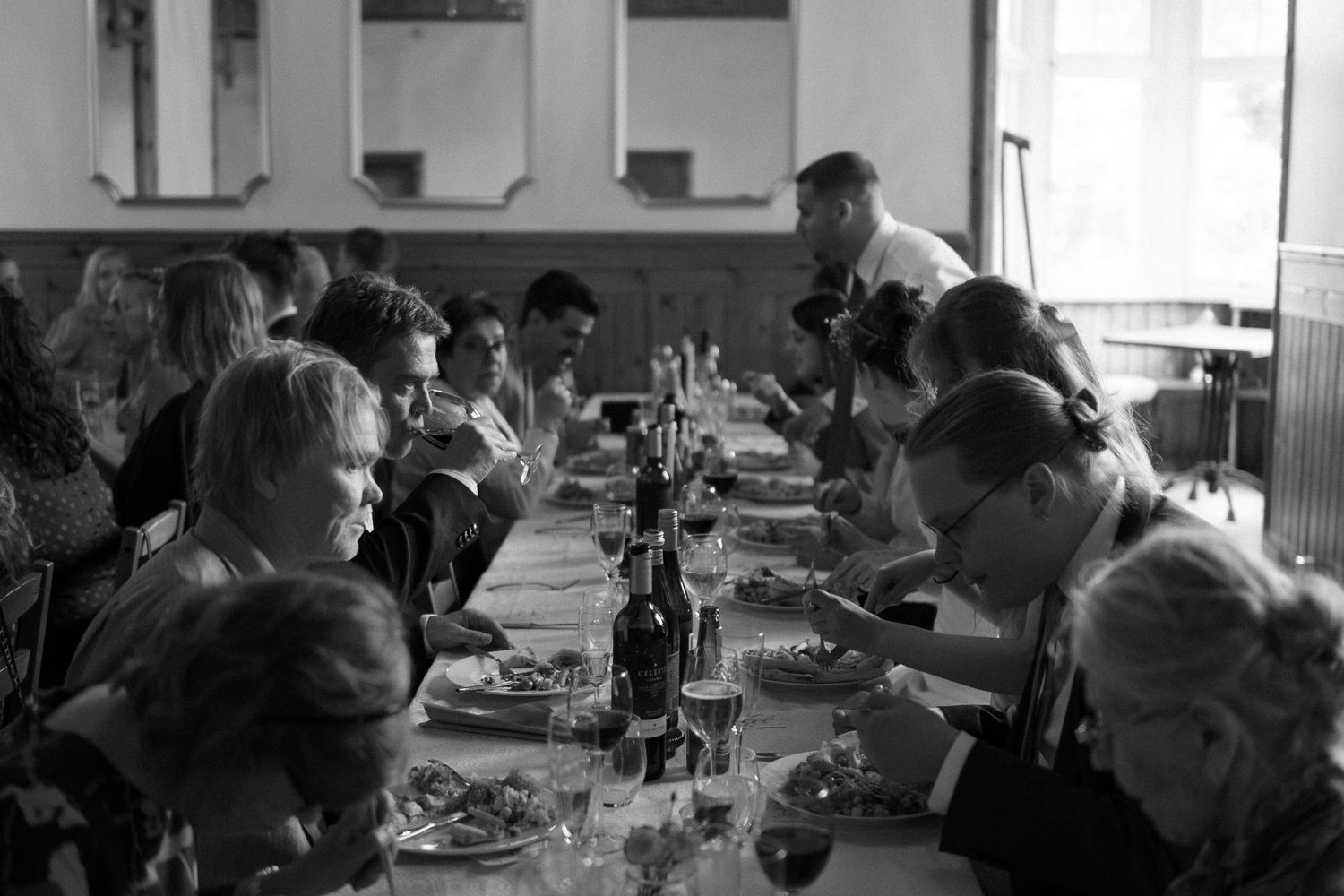 Wedding reception guests seated at long tables in a bright, airy venue with natural lighting.