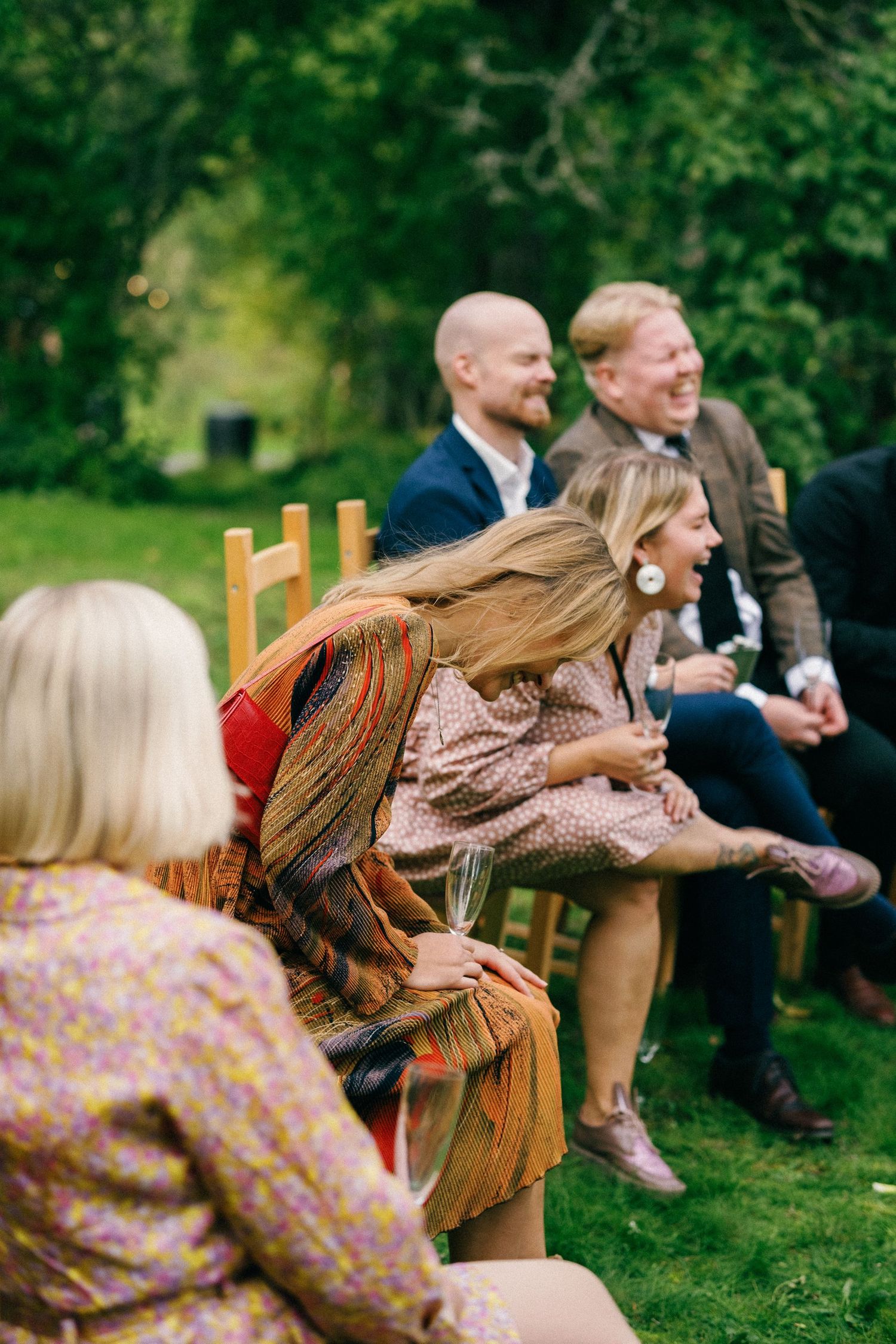 Guests enjoying a candid moment of laughter while seated on wooden chairs in a garden setting.