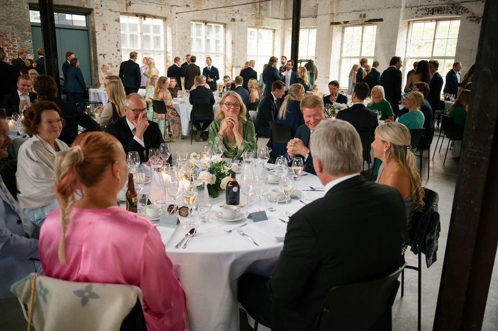 Wedding reception guests seated at elegant round tables in a bright indoor venue.
