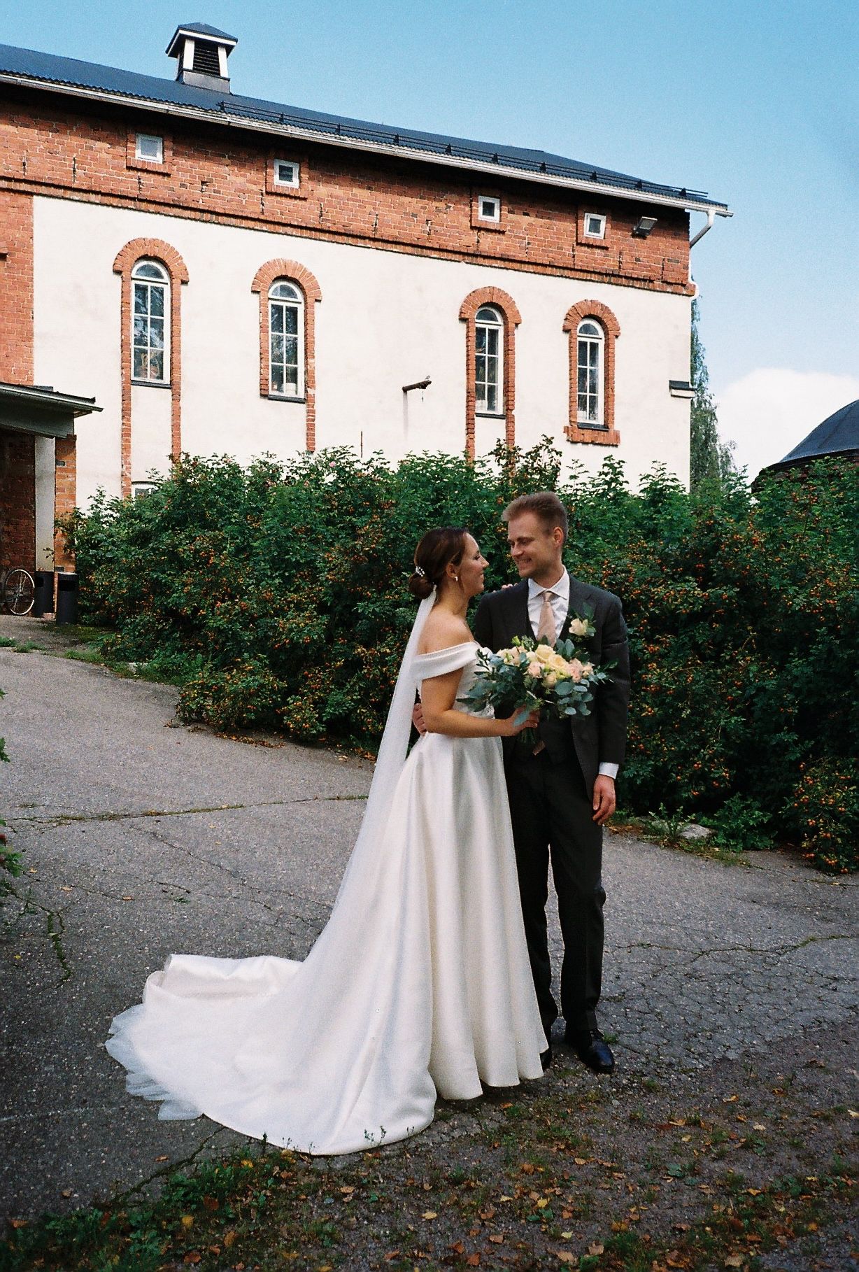 Wedding couple poses in front of historic brick building with rose bushes.