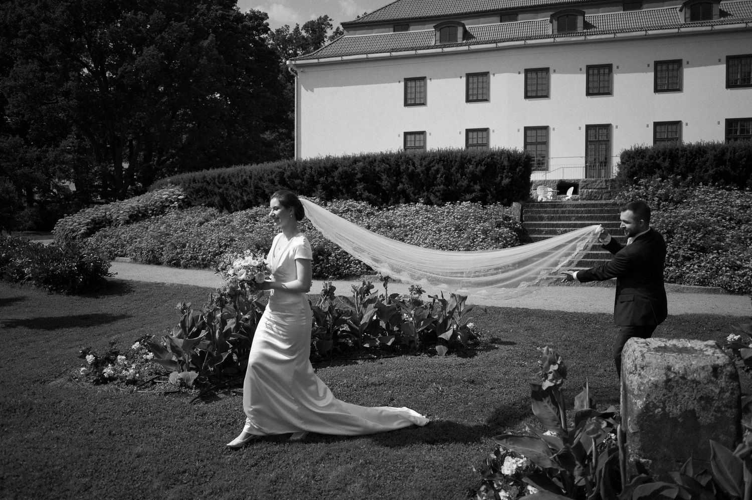 Black and white photo of a bride with flowing dress in a garden setting.
