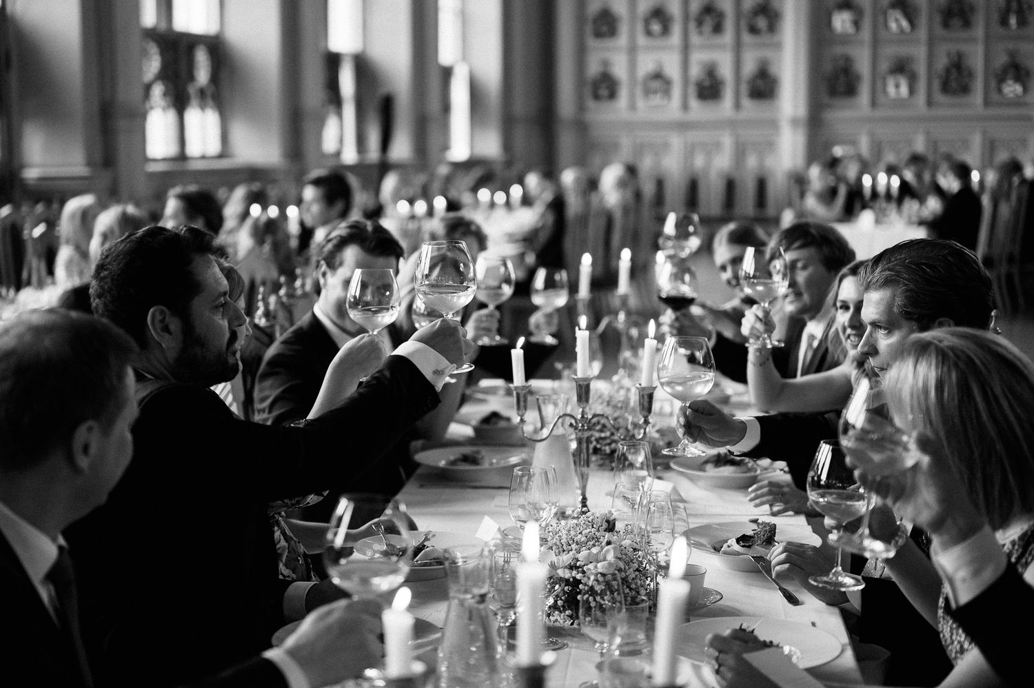 A black and white photo of a formal dining event with guests seated at long tables with elegant place settings and candles.