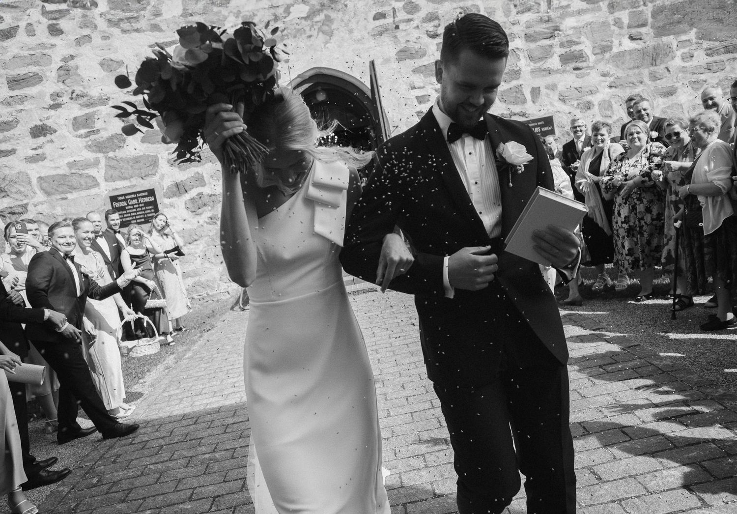 Black and white photo sequence showing a couple dancing together at a wedding celebration against a stone wall backdrop.