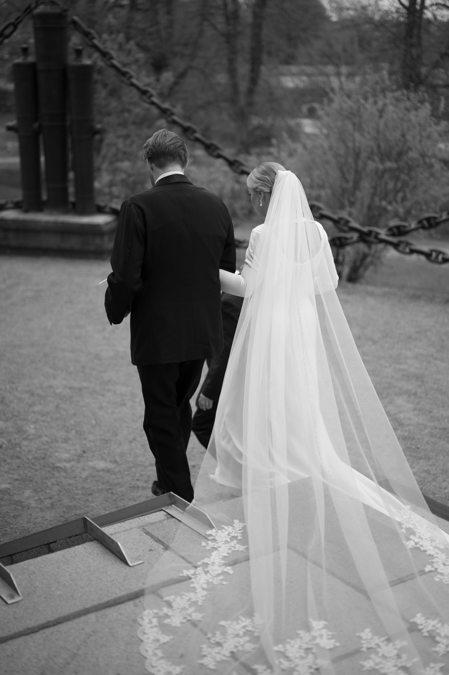A series of black and white wedding photos showing a couple walking up stone steps with the bride's veil trailing behind.