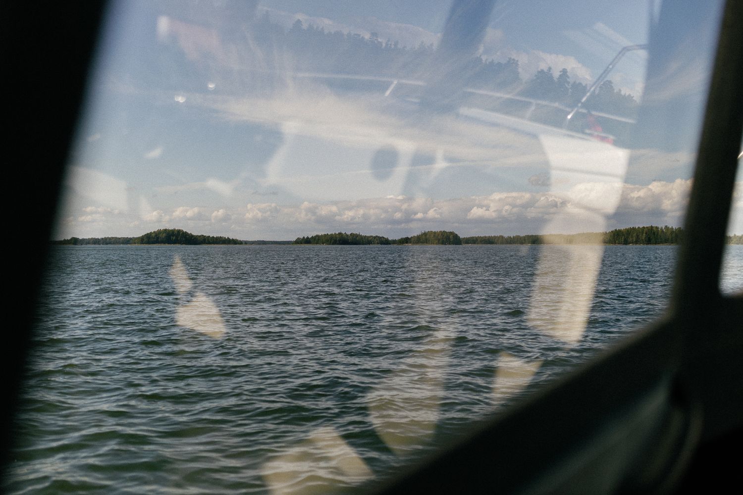 Scenic lake view through a boat window showing islands and reflective water.