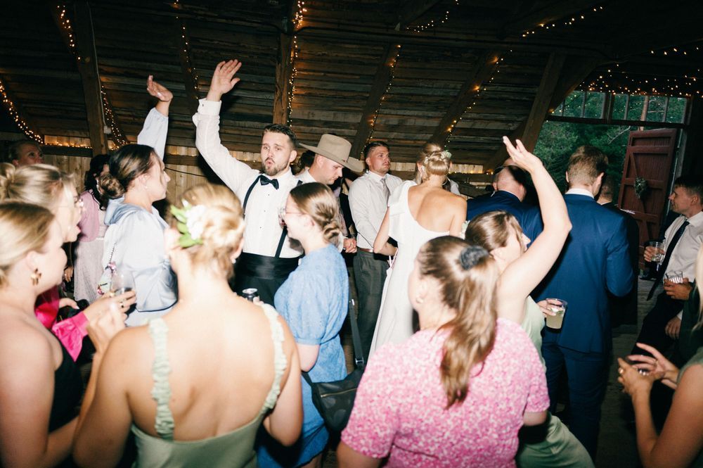 Energetic crowd dancing with raised arms under string lights at an indoor celebration.