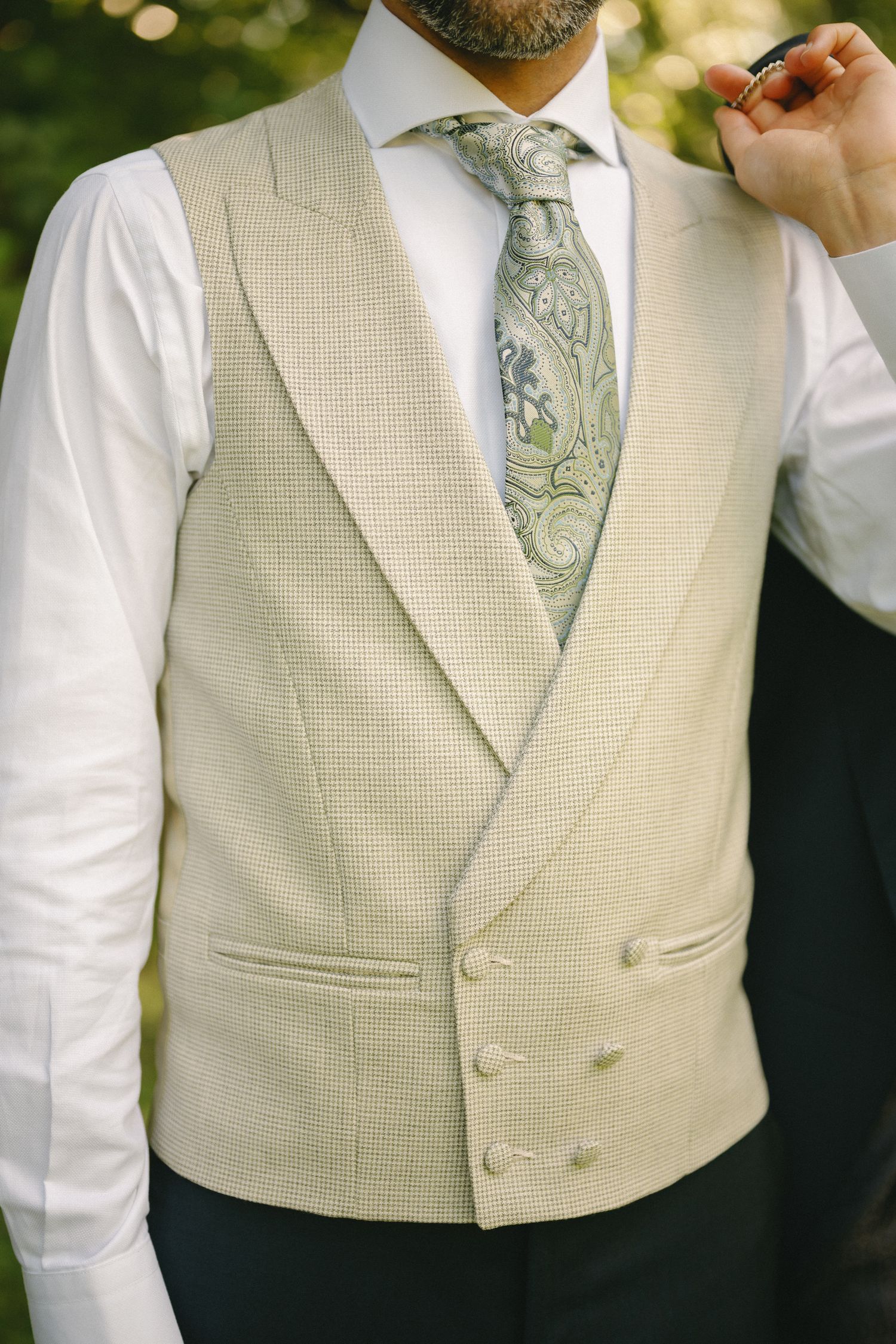 Man wearing a cream double-breasted vest with white shirt and green paisley tie at a formal event.