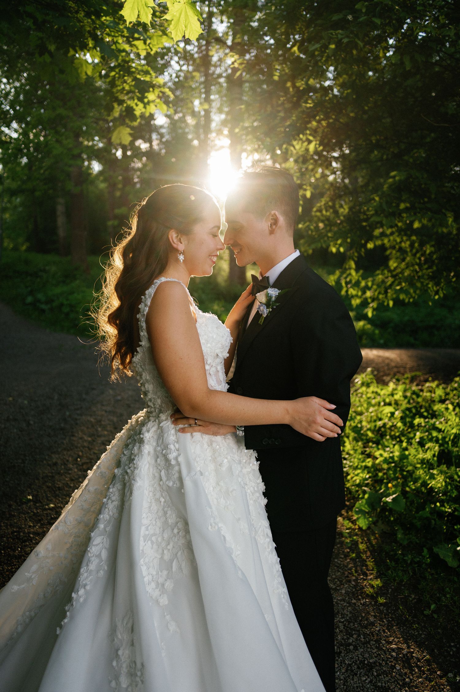 Wedding couple embracing in sunlit garden with backlit foliage.