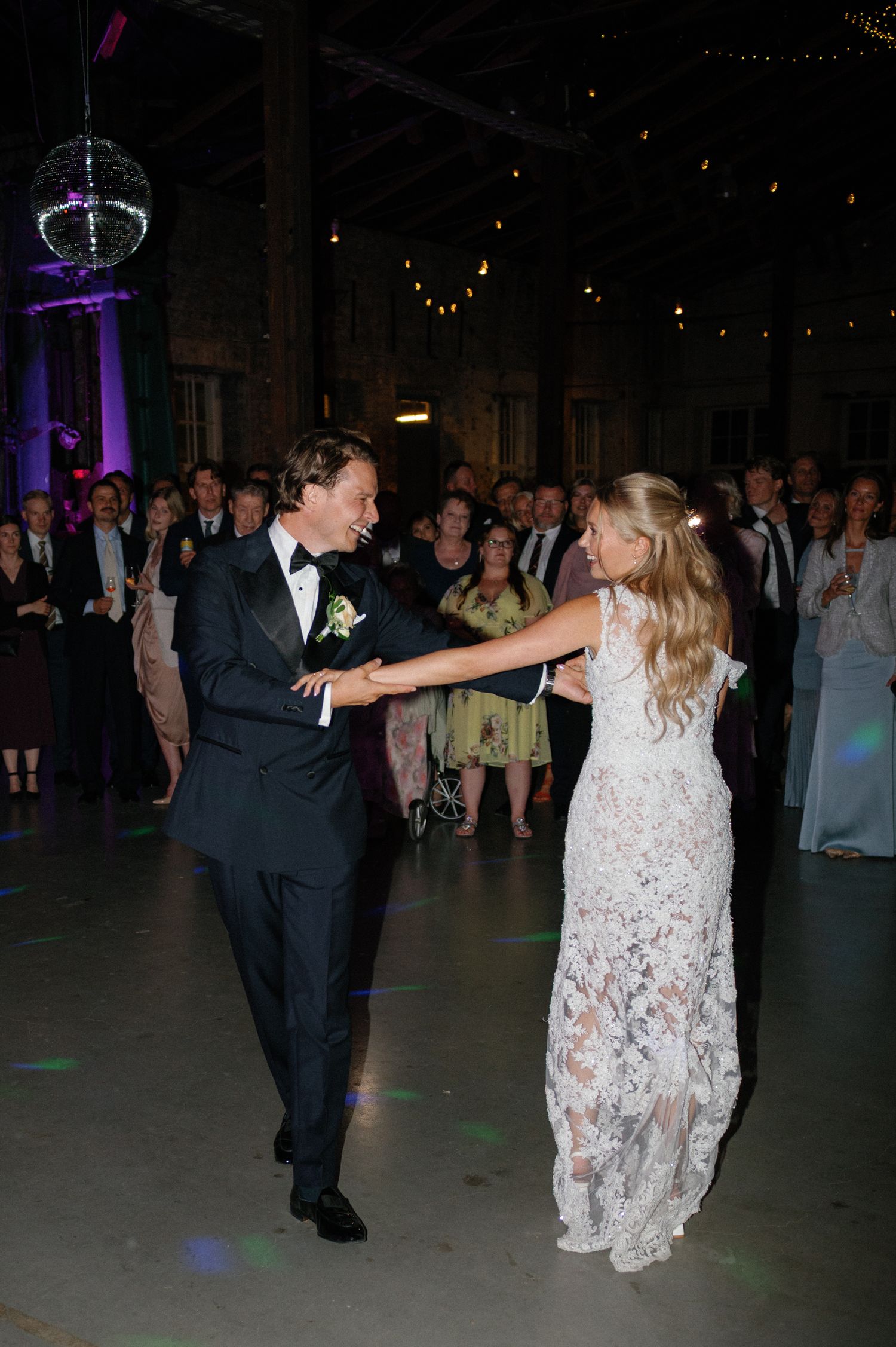 Wedding couple dancing energetically at reception with purple lighting.