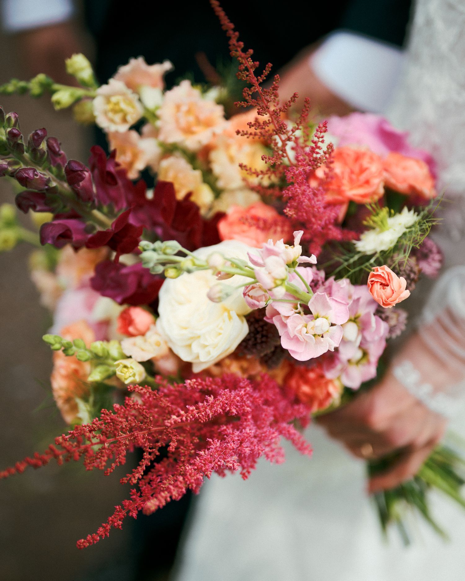 Vibrant wedding bouquet featuring pink astilbe, peach roses, and mixed seasonal flowers.