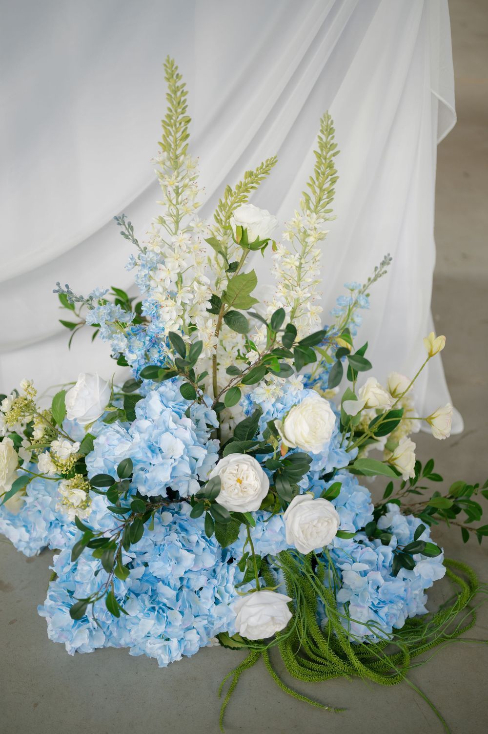 Elegant floral arrangement featuring blue hydrangeas, white roses, and delicate greenery.