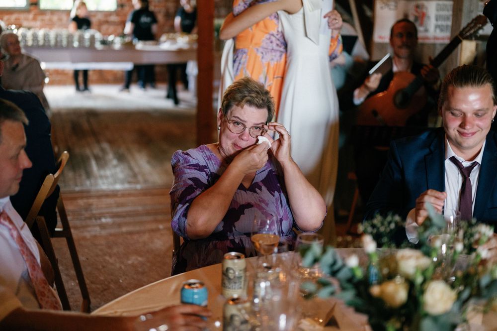 Wedding guests enjoying a reception celebration at rustic wooden tables with decorative floral centerpieces.