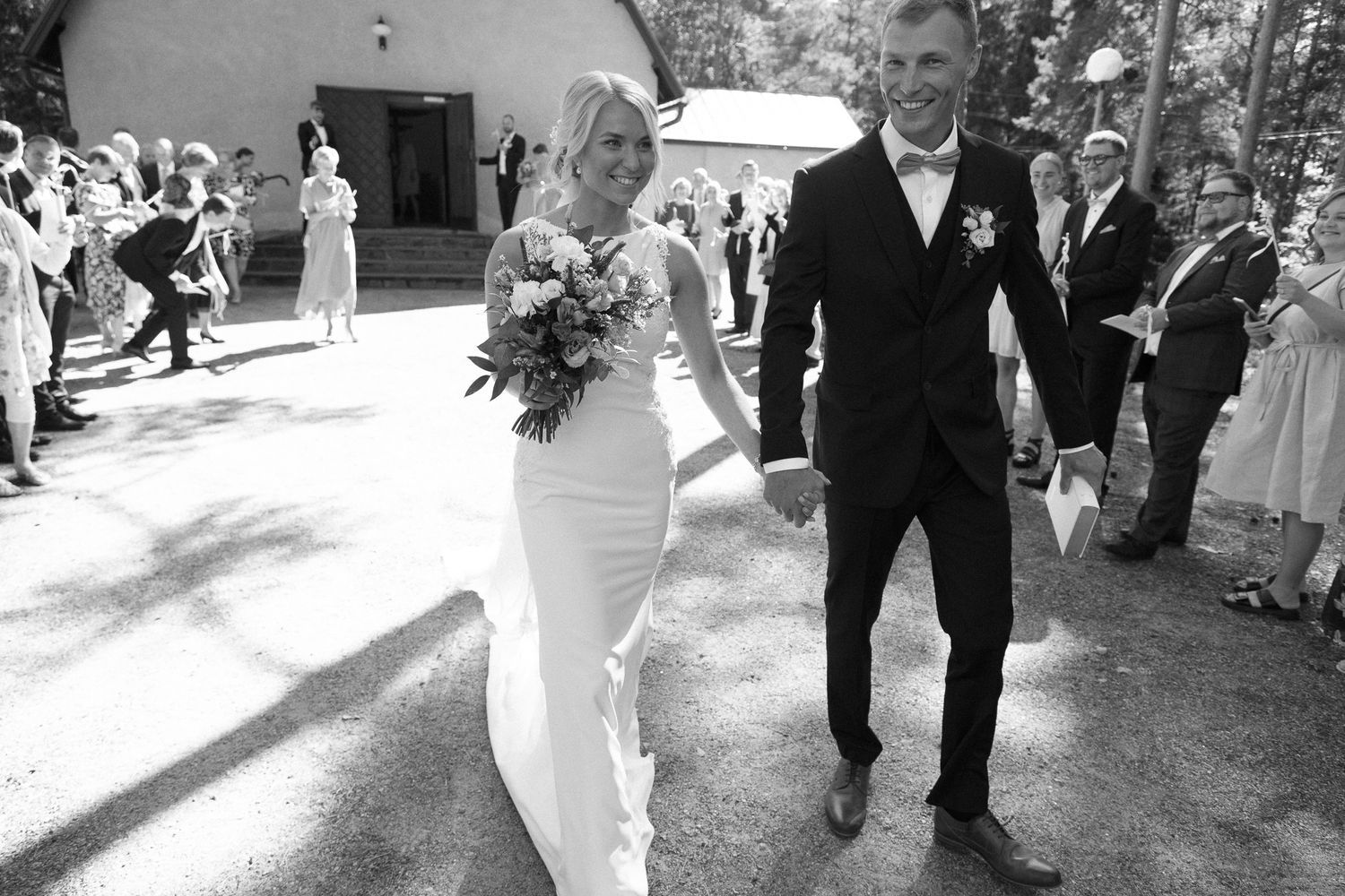 Black and white photo of wedding guests celebrating outside a rustic chapel.