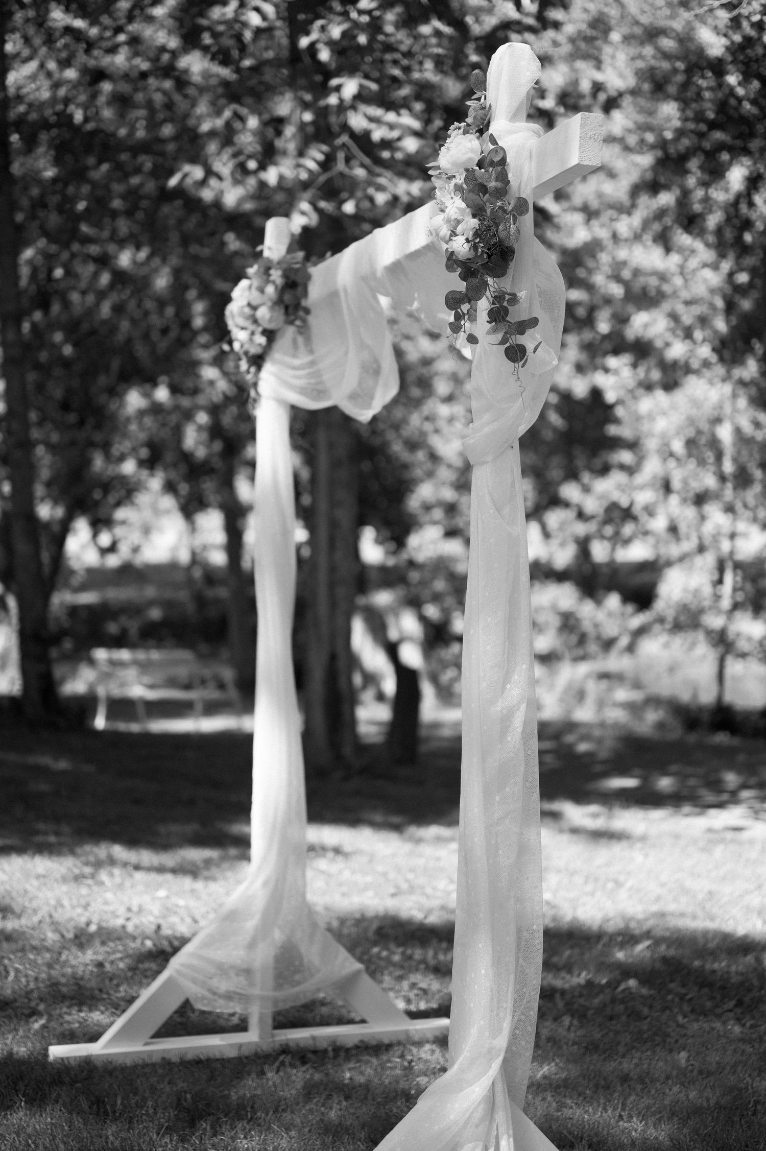 White fabric draped wedding arch decorated with flowers in outdoor garden setting.