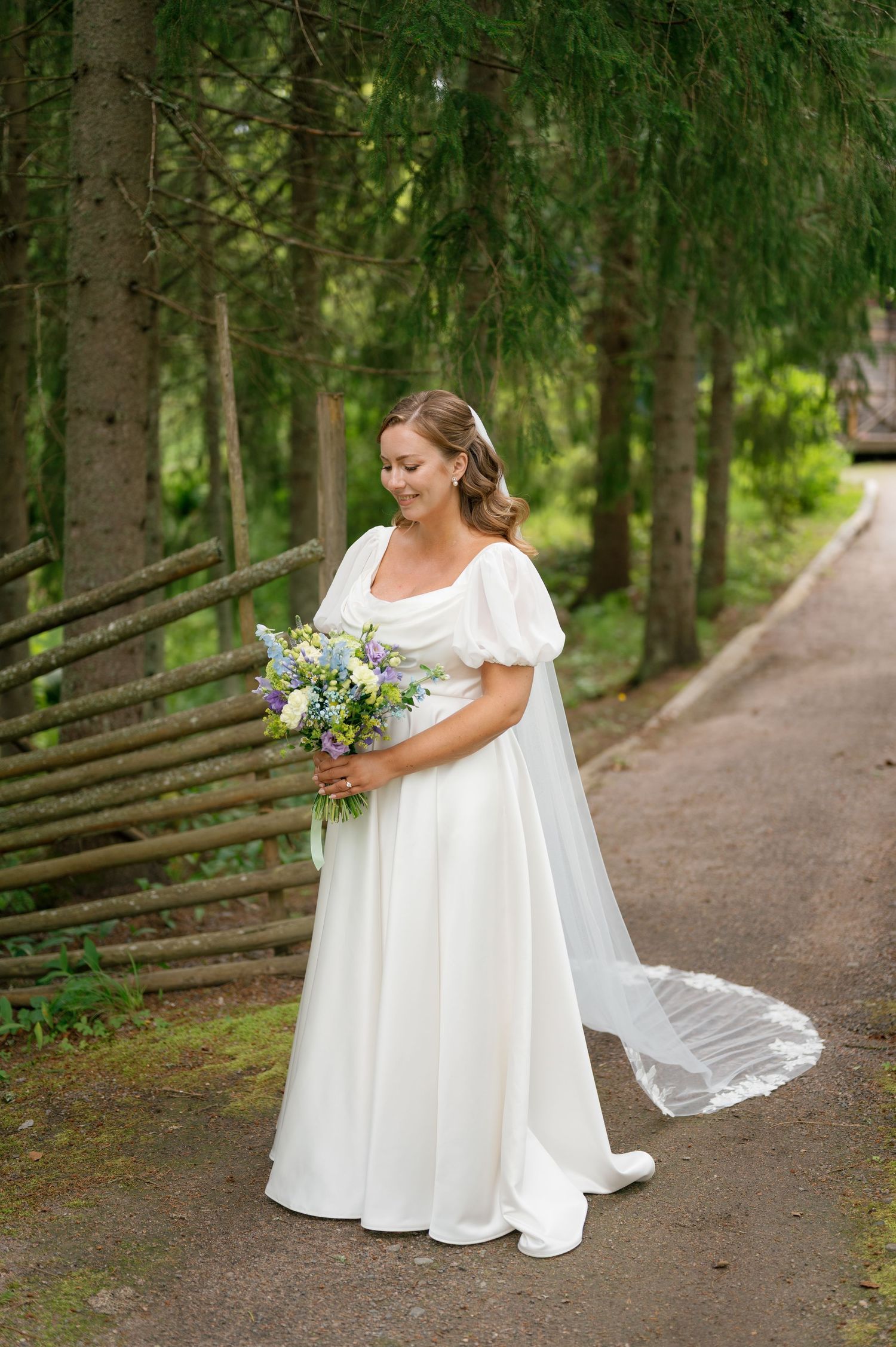 Bride holding bouquet while walking on forest path in flowing white dress.